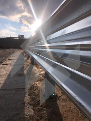 Sunshine shining through between the clouds in the sky and the 3-wave guardrail on the ground, showing the new vehicle restraint system in a beautiful play of light and shadow.